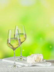 Two glasses of white wine served with cheese board on light green background. Wine mood concept