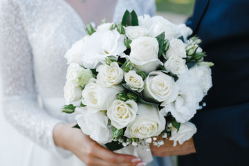 bride and groom hold a bouquet of brides from white roses