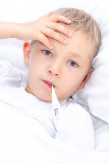 boy lies in bed with a thermometer in his mouth. healthcare concept and sick child, coronavirus, high fever, vertical photo