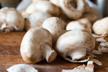 Fresh champignon mushrooms on the old wooden cutting board ready for frying. Side view. Close-up.