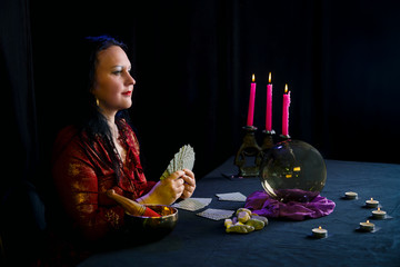 Young clairvoyant and fortuneteller with cards in hands in a magic salon on a black background.