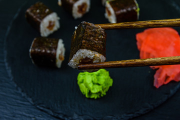Sushi maki roll with tuna, wasabi and ginger on a slate board. Chopsticks with sushi roll. Japanese food