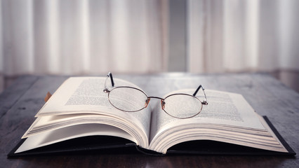 Open book over wooden table with glasses on it. Library. Literature. Read. Study.