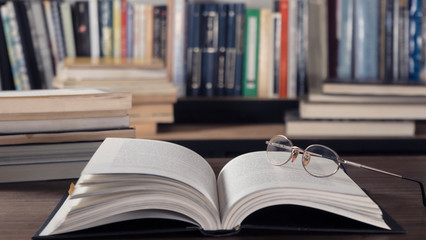 Open book over open book in library full of stacks of books with glasses over it. Library, Read. Edication. Literature.
