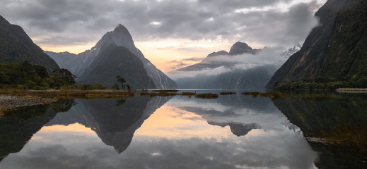 Panoramic landscape shot of sunrise in fjord with peaks shrouded in clouds and perfectly still...
