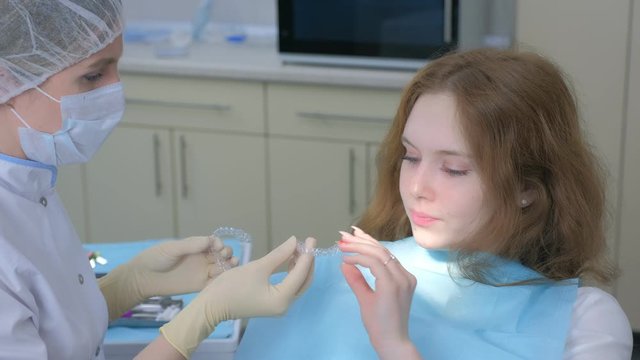 Orthodontist doctor putting silicone invisible transparent braces in girl's teeth in stomatology clinic. Portrait of teen girl. Correcting teeth. Oral hygiene and treatment, cure in dentistry.