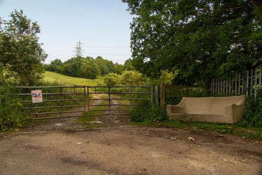 a couch fly tipped on a roadside near to a sign warning against tipping waste, in a countryside location.