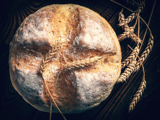 Homemade round bread. Top view of a loaf of warm fresh peasant bread and wheat spikelets on a wooden background. Homemade baking.