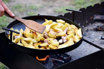 Potato roasting on frying pan on open fire on charcoal on barbecue
