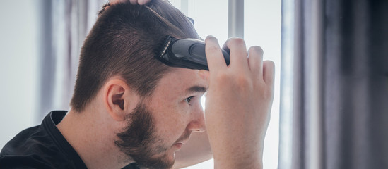 man with a beard cuts and cares for the hair himself in a quarantine coronavirus pandemic covid 19, the concept of stay home, a home hairdresser