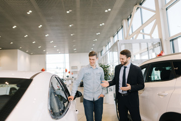 Cheerful automobile seller wearing business suit is telling interested buyer wearing casual clothes...