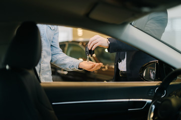 Close-up of car salesman handing over keys for new car to young man buyer in auto dealership, view...