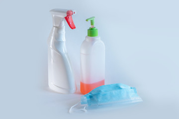 The bottle spray of white color with the red button, a liquid soap and medical mask is on a table of the white color, a set during a pandemic for disinfection, protection of respiratory system