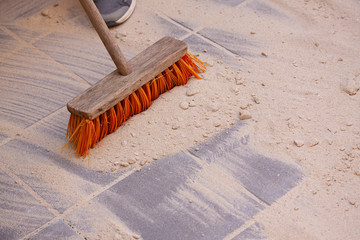 Sand spread over the surface of pavers or tiles and sweeping it into the spaces with a broom. Close...