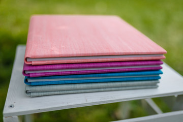 Spines of books, albums, notebooks or photobooks with grey, turquoise, purple and pink leather covers lying on white wooden box among green grass. Soft focused close up shot.