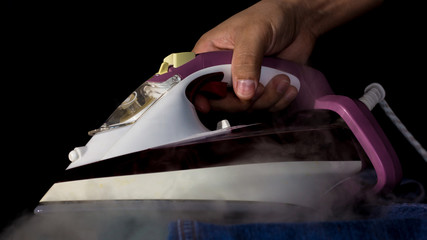 A hand holds an iron from which steam flows. Ironing concept.