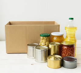 Cardboard box and various food for donation on a white wooden table. Food donations or delivery concept.