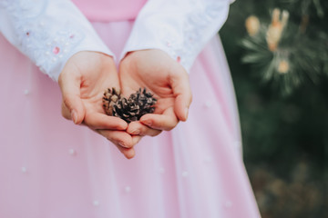 The girl in a pink dress holds cones in the hands of the forest