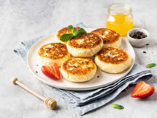 Cottage cheese pancakes, syrniki, ricotta fritters on ceramic plate with honey, chocolate and fresh strawberry. Healthy and delicious morning breakfast. Copy space. Grey concrete background. 
