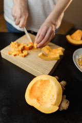 Woman chopping pumpkin on kitchen board, only hands visible. Autumn seasonal vegetables cooking. Healthy eating habits, organic vegetarian food concept.