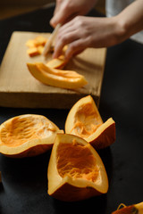 Woman chopping pumpkin on kitchen board, only hands visible. Autumn seasonal vegetables cooking. Healthy eating habits, organic vegetarian food concept.