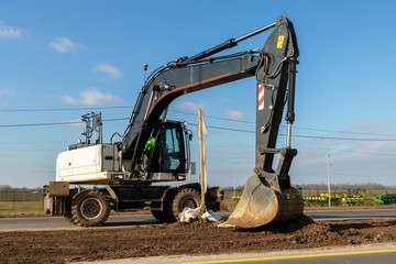 Big white modern wheeled excavator digging and mowing earth at infrastructure highway road construction site. Heavy industrial machinery at work backgruond. Automotive digger machine