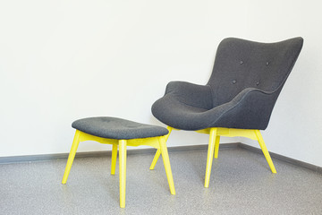 gray chair with wooden yellow legs and a gray footrest with yellow wooden legs
