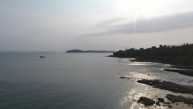 Hover Aerial Flight of Casaya Island (Las Perlas) Rocky Beach Shoreline with Sailboat at Anchor and Sun Glare