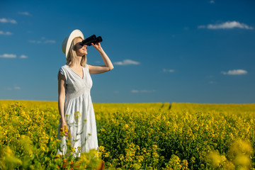Fototapeta premium Beautiful woman in dress with binoculars in rapeseed field