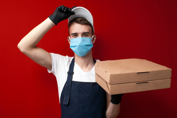 Fototapeta na wymiar guy delivers pizza in a protective mask and gloves holds boxes and shows ok, student worker delivers pizza during epidemic of coronavirus