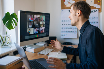 Young man having a video call via a computer in the home office. Stay at home and work from home concept during Coronavirus pandemic. Virtual house party 