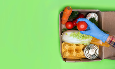
Products for donation. Volunteer in blue gloves collects parcel. Green background.