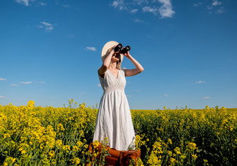 Fototapeta premium woman in dress with suitcase and binoculars in rapeseed field
