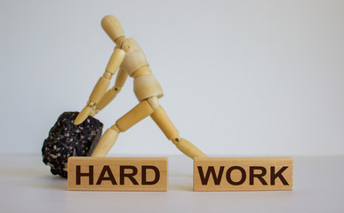 Wooden blocks with words 'hard work'. Wooden model of human with black stone.