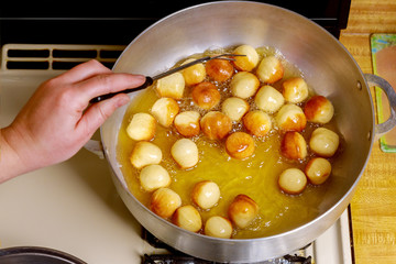 Woman fries munchkins or small donuts in hot oil.