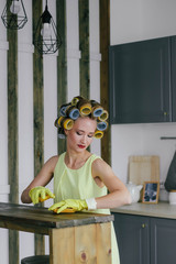 Obraz premium The girl the blonde in curlers and in a yellow dress cleans up with gloves and a sponge