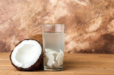 Health content, coconut water in a glass, coconut halves, brown background