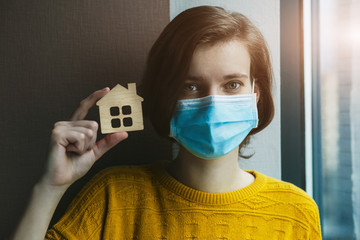 Woman in medical mask holding model go house. Stay at home symbol. Home Isolation during coronavirus pandemic concept.