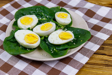 Boiled eggs with fresh spinach leaves and sesame seeds on wooden table