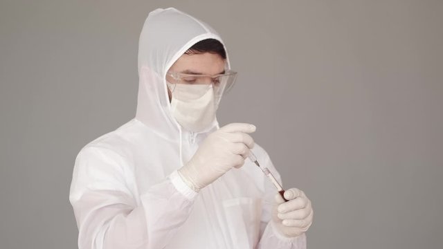 A male researcher is doing research in a laboratory. The scientist is wearing full-covering equipment as he deals with infectious liquid. The man is trying to fing the vaccine for coronairus. He is
