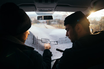 Two robbers planning and pointing on the blueprint(map) their objective while holding their guns.
