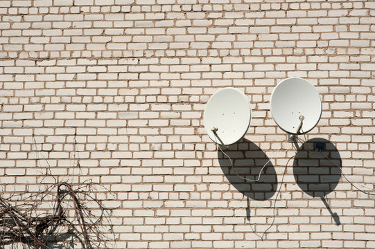 two satellite dishes on a white brick wall background © Юрий Горид