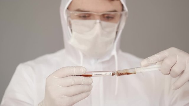 A male researcher is doing research in a laboratory. The scientist is wearing full-covering equipment as he deals with infectious liquid. The man is trying to fing the vaccine for coronairus. He is