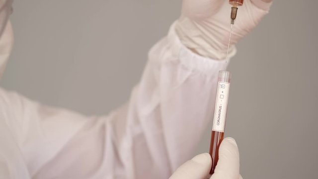 A male researcher is doing research in a laboratory. The scientist is wearing full-covering equipment as he deals with infectious liquid. The man is trying to fing the vaccine for coronairus. He is
