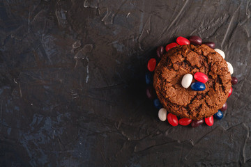 Obraz na płótnie Canvas Homemade oat chocolate cookies stack with cereal with juicy jelly beans on textured dark black background, top view copy space