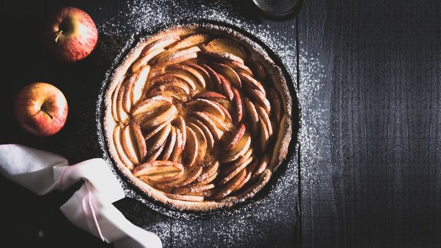 Deliciosa torta de ma&ccedil;&atilde; na panela de ferro sobre o tampo de madeira r&uacute;stico preto e mais duas lindas ma&ccedil;&atilde;s