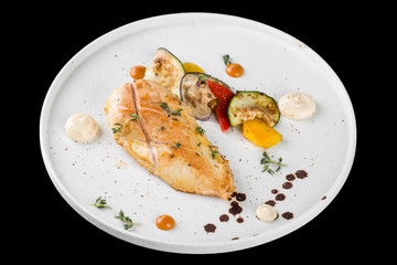 Grilled chicken breast served with baked vegetables. Isolated on a black background.