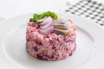 Russian salad herring under a fur coat. It is made from potatoes, carrots, beets, herring, onions. On a white plate, close up.