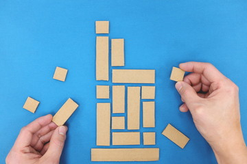 Nation rebuilding concept. Hands fixing fallen building blocks. Blue background, top view.