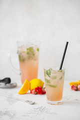 Summer refreshing cocktail with tea rose petals, lemon and mint. Refreshing drink in a glass on a light stone background with bartender tools.